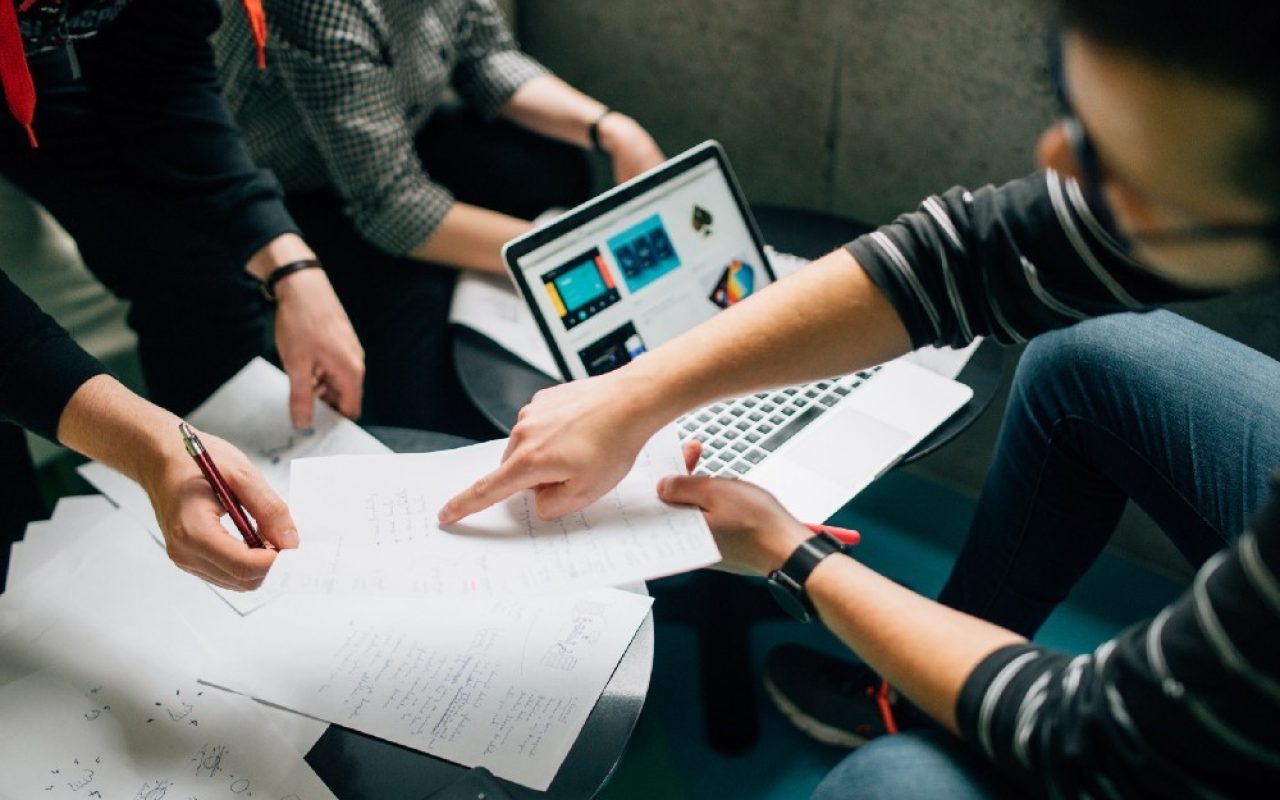three people surrounding paper and laptop inside room